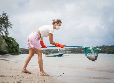 A female ecologist volunteer cleans the beach on the seashore from plastic and other waste.