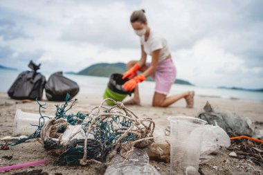 Kadın bir çevre bilimci plastikten ve diğer atıklardan sahil kenarını temizliyor..