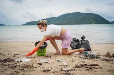 A female ecologist volunteer cleans the beach on the seashore from plastic and other waste.