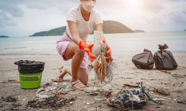 A female ecologist volunteer cleans the beach on the seashore from plastic and other waste.