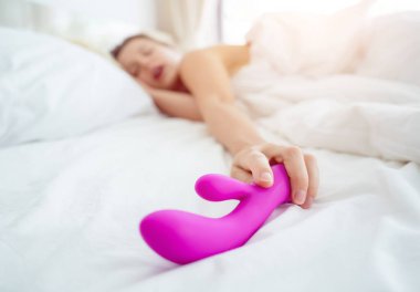 Yatakta elinde yetişkinler için bir seks oyuncağı tutan genç seksi kadın..