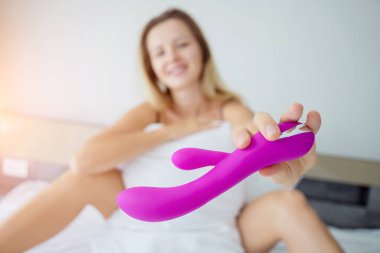 Yatakta elinde yetişkinler için bir seks oyuncağı tutan genç seksi kadın..