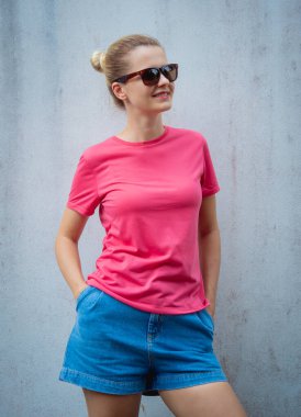 Gri bir duvarın arka planında pembe, boş tişört giyen kadın model.