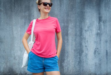 Gri bir duvarın arka planında pembe, boş tişört giyen kadın model.