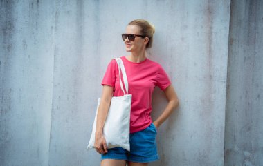 Gri bir duvarın arka planında pembe, boş tişört giyen kadın model.