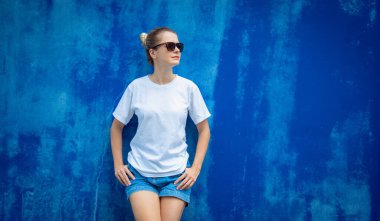 Mavi bir duvarın arka planında beyaz tişört giyen kadın model.