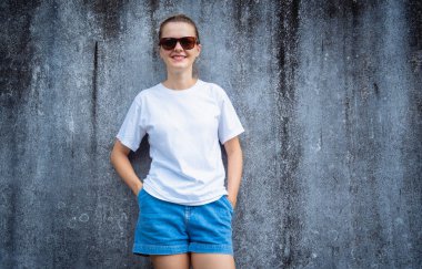 Beyaz beyaz tişört giyen kadın manken arka planda gri bir duvar çiziği var.