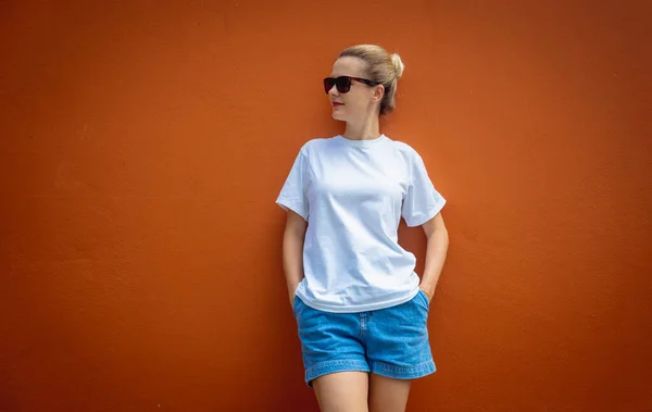 Female model wearing white blank t-shirt on the background of an orange wall