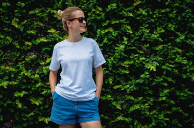 Yaprak duvarın arka planında beyaz, boş tişört giyen bir kadın model.