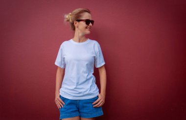 Bordo bir duvarın arka planında beyaz tişört giyen kadın model.