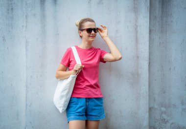 Gri bir duvarın arka planında pembe, boş tişört giyen kadın model.