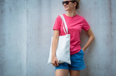 Gri bir duvarın arka planında pembe, boş tişört giyen kadın model.