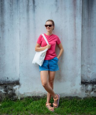 Gri bir duvarın arka planında pembe, boş tişört giyen kadın model.