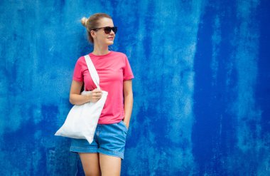 Mavi bir duvarın arka planında pembe, boş tişört giyen kadın manken.