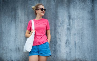 Gri bir duvarın arka planında pembe, boş tişört giyen kadın model.