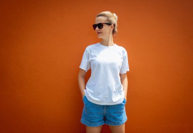 Turuncu bir duvarın arka planında beyaz tişört giyen kadın model.