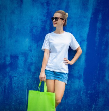 Mavi bir duvarın arka planında beyaz tişört giyen kadın model.