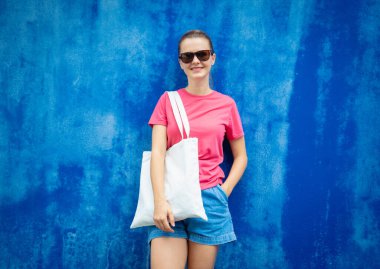 Mavi bir duvarın arka planında pembe, boş tişört giyen kadın manken.