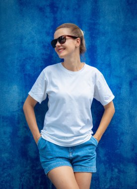 Mavi bir duvarın arka planında beyaz tişört giyen kadın model.