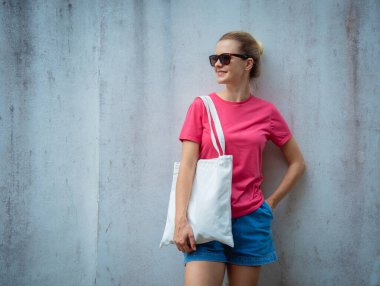 Gri bir duvarın arka planında pembe, boş tişört giyen kadın model.