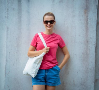 Gri bir duvarın arka planında pembe, boş tişört giyen kadın model.