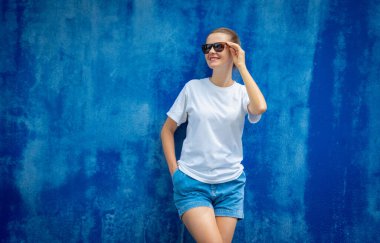 Mavi bir duvarın arka planında beyaz tişört giyen kadın model.