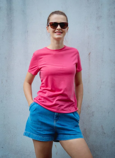 グレーの壁を背景にピンクのTシャツを着た女性モデル — ストック写真