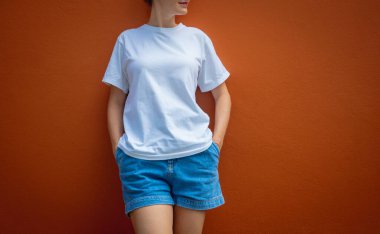 Turuncu bir duvarın arka planında beyaz tişört giyen kadın model.