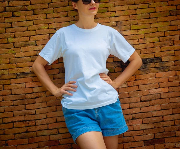 Female model wearing white blank t-shirt on the background of an bricks wall