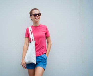 Gri bir duvarın arka planında pembe, boş tişört giyen kadın model.