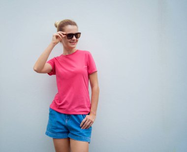 Gri bir duvarın arka planında pembe, boş tişört giyen kadın model.