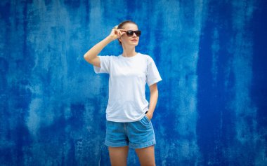 Mavi bir duvarın arka planında beyaz tişört giyen kadın model.