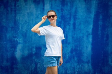 Mavi bir duvarın arka planında beyaz tişört giyen kadın model.