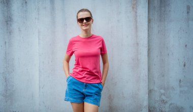 Gri bir duvarın arka planında pembe, boş tişört giyen kadın model.