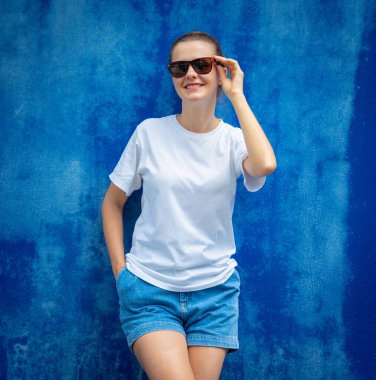 Mavi bir duvarın arka planında beyaz tişört giyen kadın model.