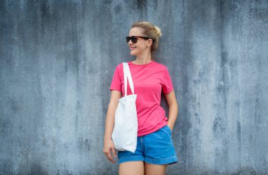 Gri bir duvarın arka planında pembe, boş tişört giyen kadın model.