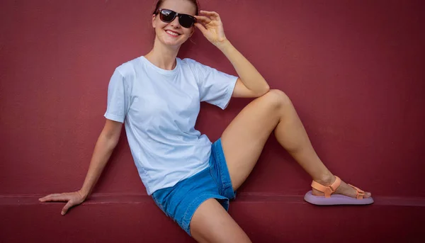 Female model wearing white blank t-shirt on the background of an burgundy wall