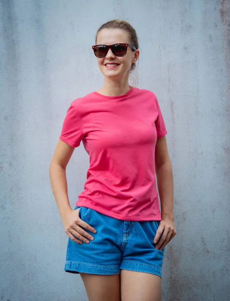 Female model wearing pink blank t-shirt on the background of an gray wall