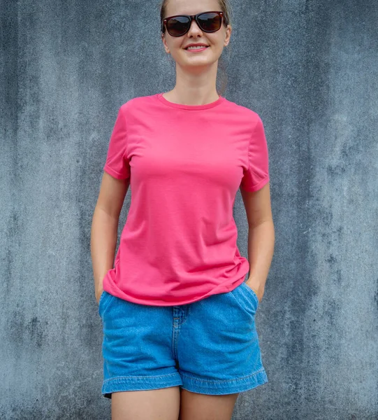 Female model wearing pink blank t-shirt on the background of an gray scratched wall