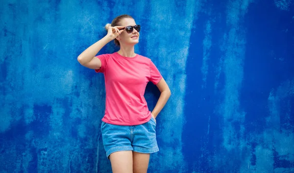Female model wearing pink blank t-shirt on the background of an blue wall