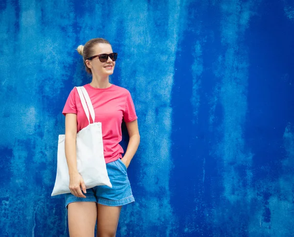 Mavi bir duvarın arka planında pembe, boş tişört giyen kadın manken.