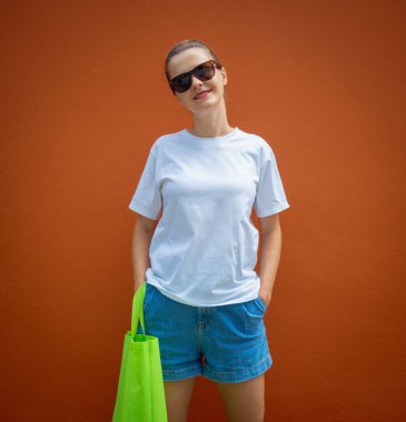 Turuncu bir duvarın arka planında beyaz tişört giyen kadın model.