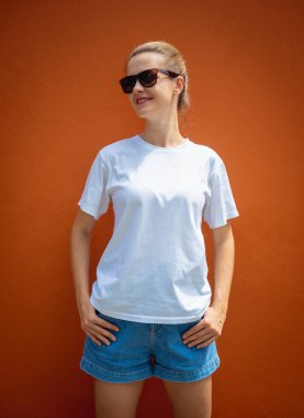 Turuncu bir duvarın arka planında beyaz tişört giyen kadın model.