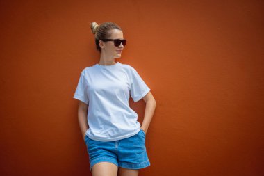 Turuncu bir duvarın arka planında beyaz tişört giyen kadın model.