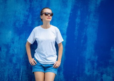 Mavi bir duvarın arka planında beyaz tişört giyen kadın model.