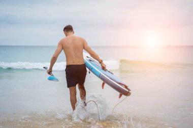 Sakin günbatımı denizinde sörf tahtası olan genç bir adam..