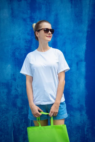 Female model wearing white blank t-shirt on the background of an blue wall