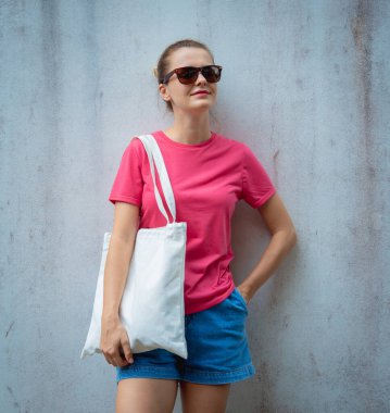 Gri bir duvarın arka planında pembe, boş tişört giyen kadın model.