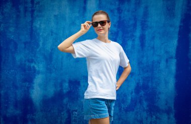 Mavi bir duvarın arka planında beyaz tişört giyen kadın model.