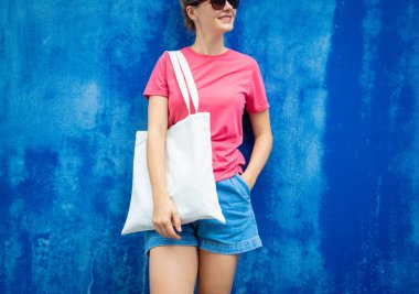 Mavi bir duvarın arka planında pembe, boş tişört giyen kadın manken.